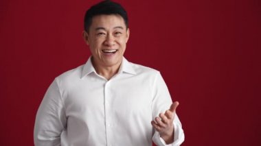Beyaz gömlekli mutlu Asyalı adam kırmızı stüdyodaki kameraya bir buket kırmızı gül uzatıyor.