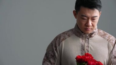 Mutlu Asyalı asker gri stüdyodaki kameraya bir buket kırmızı gül uzatıyor.