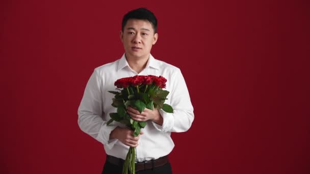 Beyaz Tişörtlü Elinde Kırmızı Güller Olan Asyalı Adam Kırmızı Stüdyoda — Stok video