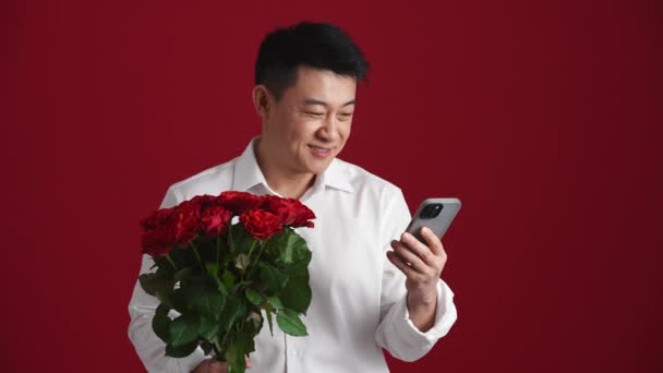 Positiv Asiatisk Man Som Håller Bukett Röda Rosor Och Skriva — Stockvideo