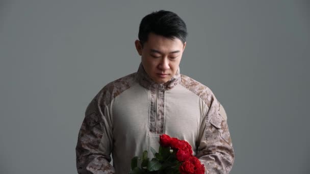 Usmívající Voják Asiat Natáhne Kameře Šedém Studiu Kytici Rudých Růží — Stock video