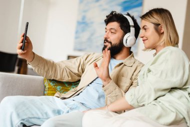 Beyaz çift evdeki kanepede otururken cep telefonu ve el kol hareketi yapıyor.
