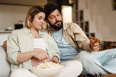 Beyaz çift evde kanepede otururken patlamış mısır yiyip film izliyor.