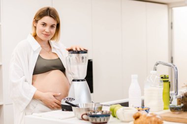 Beyaz hamile kadın gülümsüyor ve evde sulanıyor.