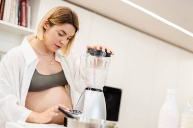 Beyaz hamile kadın evde mutfağı yumuşatıyor.