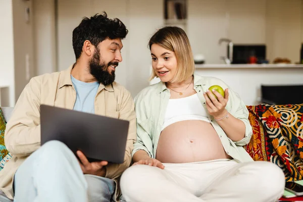 Brodaty Mężczyzna Kobieta Ciąży Pomocą Laptopa Jedzenia Jabłka Podczas Siedzenia — Zdjęcie stockowe