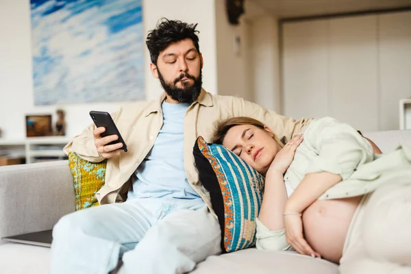 Barbudo Hombre Usando Teléfono Celular Mientras Esposa Embarazada Durmiendo Sofá — Foto de Stock