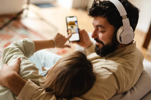Beyaz çift evdeki koltukta otururken cep telefonu ve kulaklık kullanıyor.