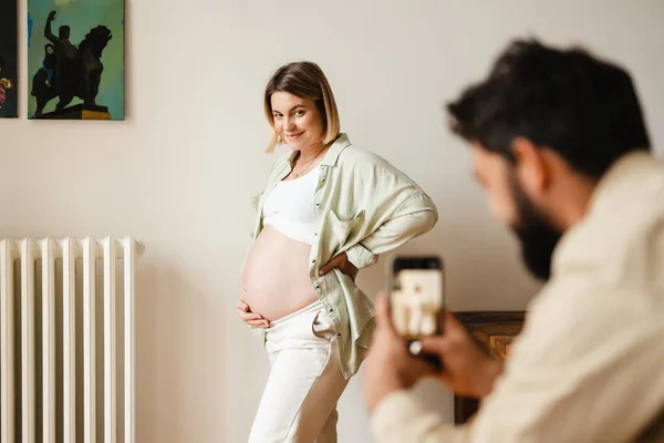 Λευκός Άντρας Φωτογραφίζει Την Χαμογελαστή Έγκυο Γυναίκα Του Στο Σπίτι — Φωτογραφία Αρχείου
