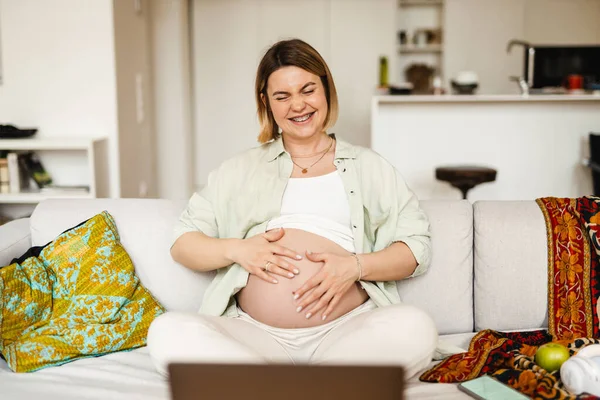 Mujer Embarazada Joven Riendo Utilizando Ordenador Portátil Mientras Está Sentado — Foto de Stock