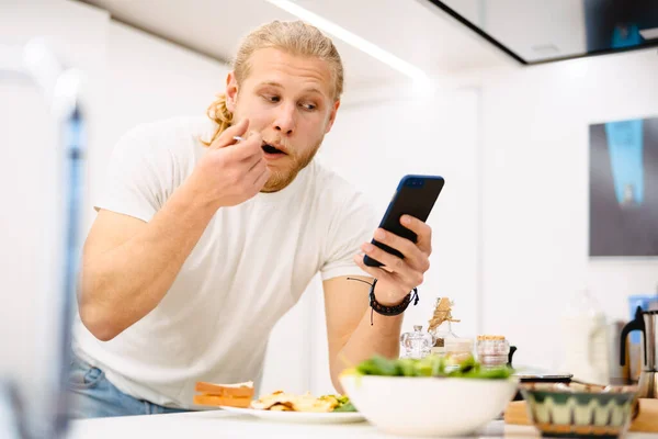 Jovem Homem Branco Usando Celular Enquanto Almoça Cozinha Casa — Fotografia de Stock