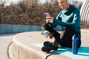 Dışarıda çalışırken cep telefonu kullanan protezli genç bir sporcu.
