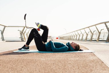 Protezli genç sporcu kadın şehir köprüsünde çalışırken egzersiz yapıyor.