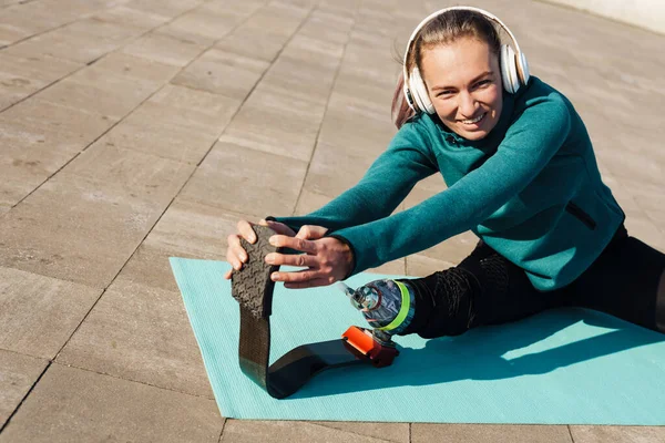 Smiling sportswoman with prosthetic leg wearing headphones sitting