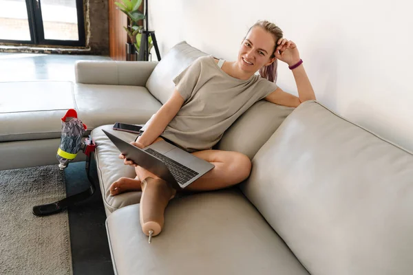 Hymyilevä Nuori Valkoinen Vammainen Nainen Proteettinen Jalka Istuu Sohvalla Kannettavan — kuvapankkivalokuva