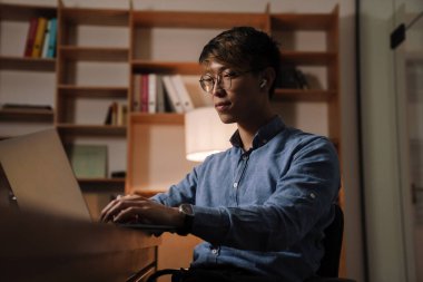 Ofiste otururken bilgisayarla çalışan kulaklıklı Asyalı adam.