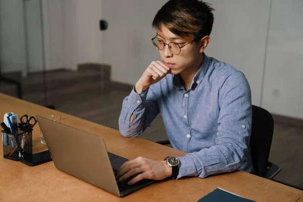 Focado Asiático Cara Óculos Trabalhando Com Laptop Enquanto Sentado Mesa — Fotografia de Stock