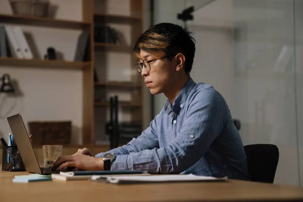 Орієнтований Азіатський Хлопець Окулярах Працює Ноутбуком Сидячи Столом Офісі — стокове фото