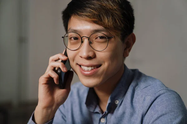 オフィスで働く中で携帯電話で話す眼鏡の幸せなアジアの男 — ストック写真