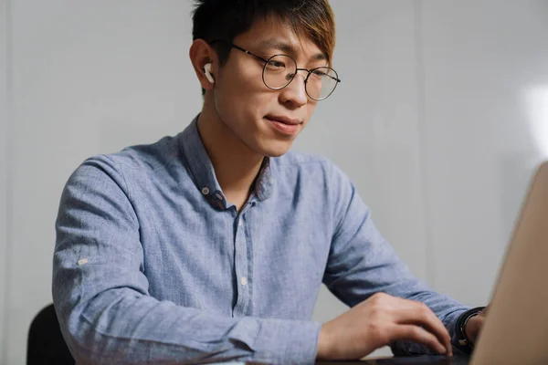 Agradado Asiático Cara Fones Ouvido Trabalhando Com Laptop Enquanto Sentado — Fotografia de Stock
