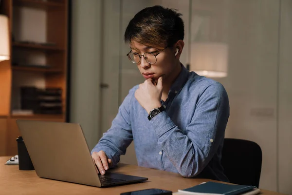 Focado Asiático Cara Fones Ouvido Trabalhando Com Laptop Enquanto Sentado — Fotografia de Stock