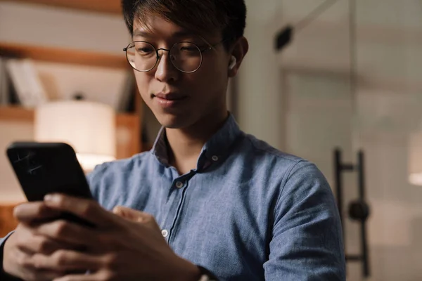 Fokuserad Asiatisk Kille Hörlurar Med Mobiltelefon När Arbetar Kontoret — Stockfoto