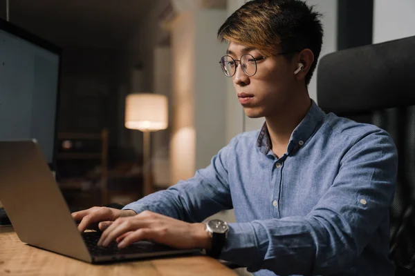 Focado Asiático Cara Fones Ouvido Trabalhando Com Laptop Enquanto Sentado — Fotografia de Stock