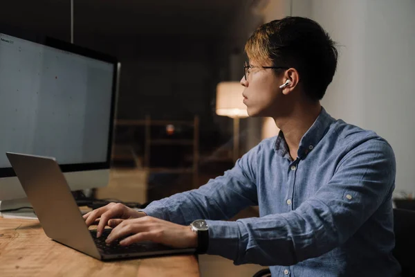 オフィスでラップトップとコンピュータを扱うイヤホンに焦点を当てたアジアの男 — ストック写真