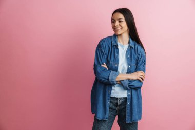 Kollarını kavuşturup pembe duvarın üzerinde poz veren genç İspanyol kadın.