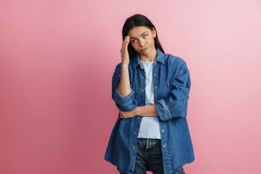 Genç İspanyol hoşnutsuz kadın yüzünü buruşturuyor ve pembe duvarın üzerinde soyutlanmış bir şekilde yukarıya bakıyor.