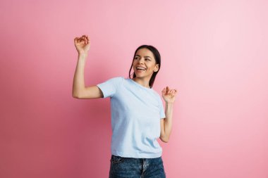 Esmer, İspanyol bir kadın pembe duvarın üzerinde dans edip şarkı söylüyor.