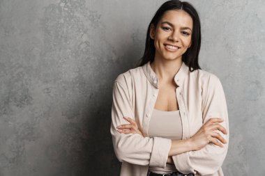 Esmer, Latin bir kadın, gri duvarın üzerinden izole edilmiş kameraya bakıp gülümsüyor.