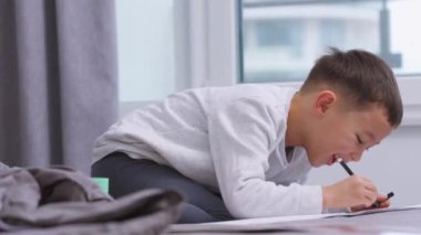 Evdeki yatağa resim çizen Asyalı gülen küçük çocuk.