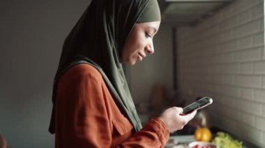 Yakışıklı Müslüman kadın mutfakta telefonla yazıyor.
