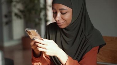 Düşünceli Müslüman kadın evde telefonla mesaj atıyor.