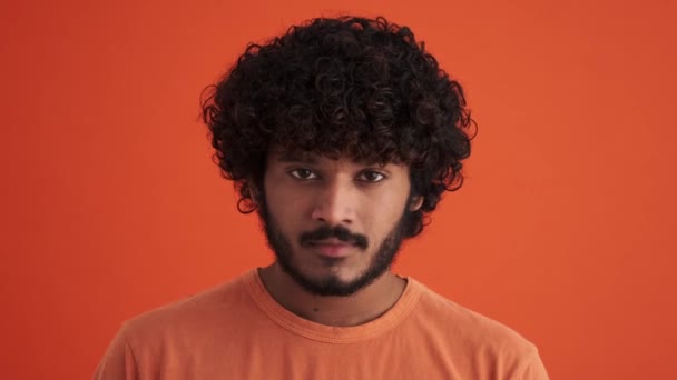 Fröhlich Lockiger Indischer Mann Blickt Orangefarbenen Studio Die Kamera — Stockvideo