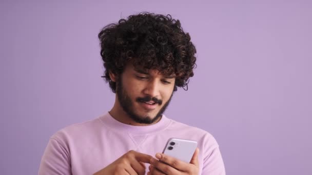 Сміючись Кучерявим Індійським Чоловіком Який Дивиться Телефон Пурпуровій Студії — стокове відео