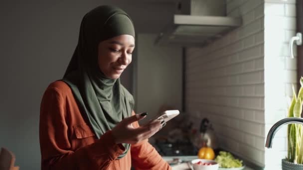 Смеющаяся Мусульманка Печатает Телефону Смотрит Окно Кухне — стоковое видео