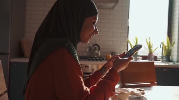 快乐的穆斯林妇女在家里用电话发短信 — 图库视频影像