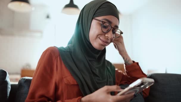 Mujer Musulmana Guapo Usando Anteojos Mensajes Texto Por Teléfono Sofá — Vídeos de Stock