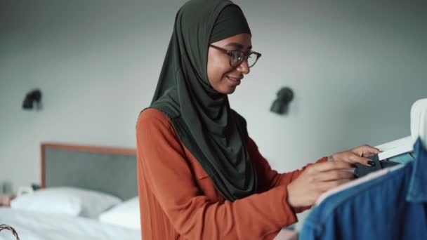 Mulher Feliz Muçulmana Vestindo Óculos Escolhe Roupas Cabide Casa — Vídeo de Stock