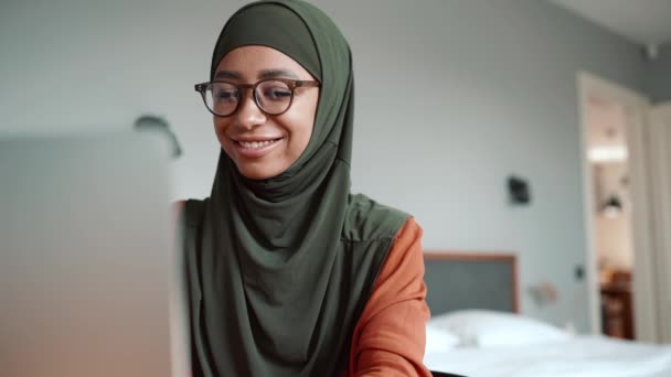穆斯林微笑的女人 戴着眼镜 用笔记本电脑打字 看着家里的相机 — 图库视频影像