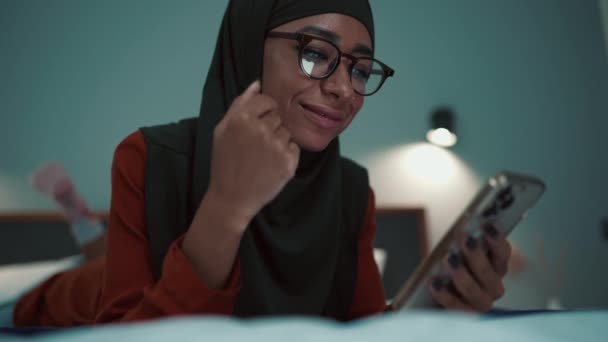 Pensiva Mulher Árabe Vestindo Óculos Digitando Telefone Cama Casa — Vídeo de Stock