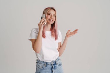 Beyaz arka planda izole edilmiş cep telefonuyla konuşurken el kol hareketi yapan genç bir kadın.
