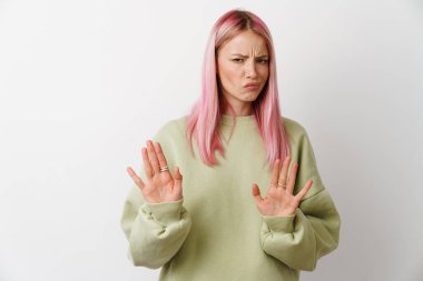 Pembe saçlı genç bir kadın beyaz arka planda izole edilmiş kameraya dur işareti yapıyor.