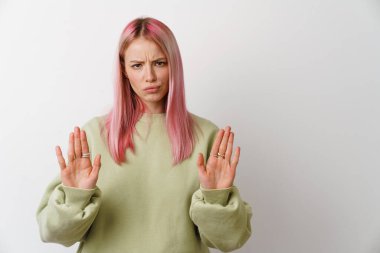 Pembe saçlı genç bir kadın beyaz arka planda izole edilmiş kameraya dur işareti yapıyor.