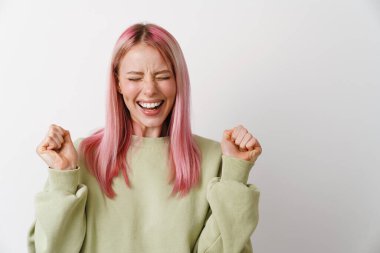 Pembe saçlı genç beyaz kadın gülüyor ve yumruklarını beyaz arka planda tutuyor.