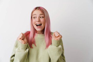 Pembe saçlı genç beyaz kadın gülüyor ve yumruklarını beyaz arka planda tutuyor.