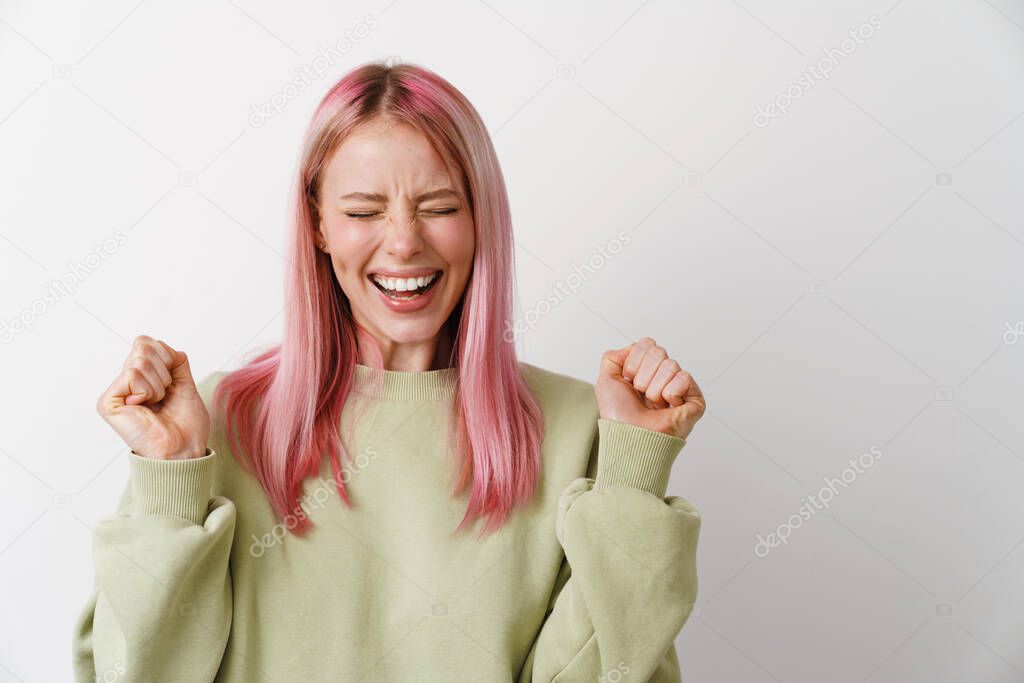 Young white woman with pink hair laughing and clenching her fists isolated over white background