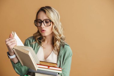 Gözlüklü güzel bir kadın. Bej duvarda izole edilmiş kitap okuyor.